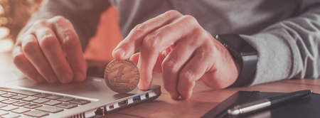Entrepreneur trading with Litecoin cryptocurrency, conceptual image of male person holding golden coin in front of laptop computerの写真素材
