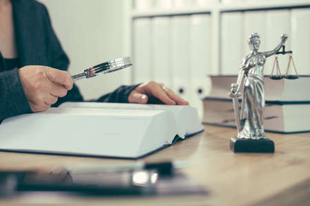 Attorney woman using magnifying glass for law book reading at her office desk, selective focusの写真素材