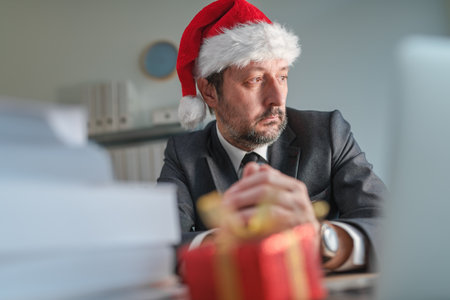 Concerned businessman with Santa Claus hat looking out the office window at Christmas holiday season, selective focusの写真素材