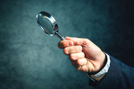 Business analytics and statistics using a magnifying glass, businessman holding vintage tool for...