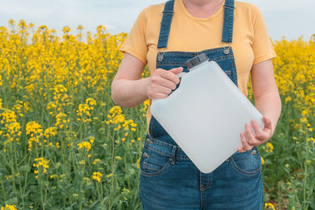 Rapeseed crop protection concept, female farmer agronomist holding jerry can bottle container with pesticide, selective focusの写真素材