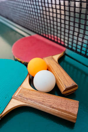 Table tennis rackets and balls on green table surface with net, selective focus