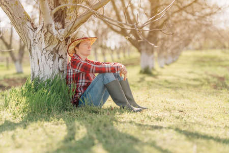 Female farmer relaxing and resting in organic walnut orchard, sitting under the fruit tree in...