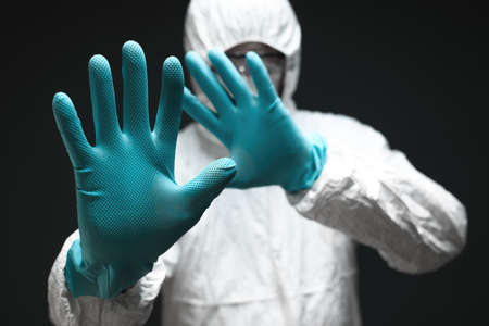Medical professional dressed in full protective coverall clothing gesturing stop sign with hands in...