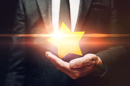 Businessman holding shiny star award in hand, customer review concept, selective focusの写真素材