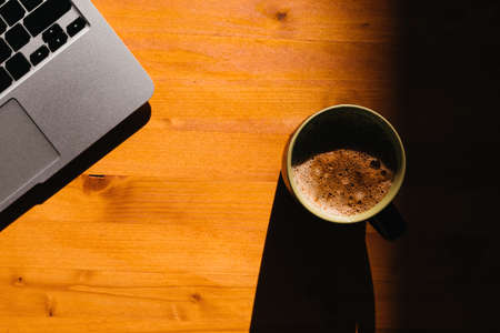 Coffee break in the office, laptop computer and coffee cup on the desk, top view with selective focusの写真素材