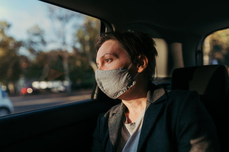 Worried businesswoman with protective face mask waiting in the car and looking out the window, selective focusの写真素材