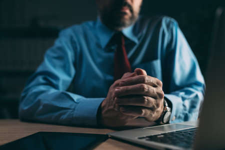 Businessman rubbing hands as body language sign of anxiety in dark office interior, selective focusの写真素材