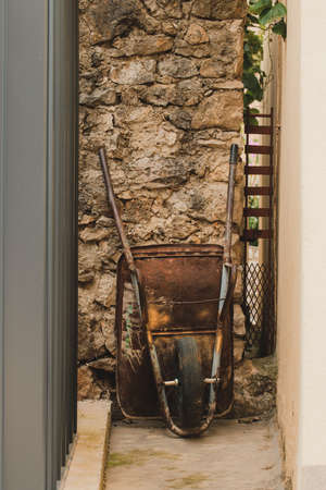 Worn garden cart wheelbarrows behind the house leaning on the wall
