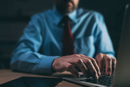 Businessman using laptop computer in dark office interior, selective focus