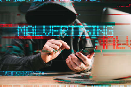 Malvertising - phone hack and attack method concept. Cyber criminal hacker using laptop and...