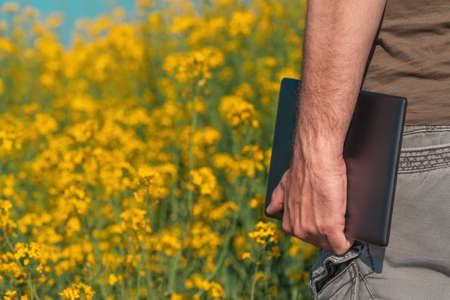 Male farmer using tablet in rapeseed field for digital tax record keeping, selective focus