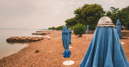 Closed beach parasol at empty seaside coast in Crikvenica, Croatia. Bad weather and rainy morning at the sea.の写真素材