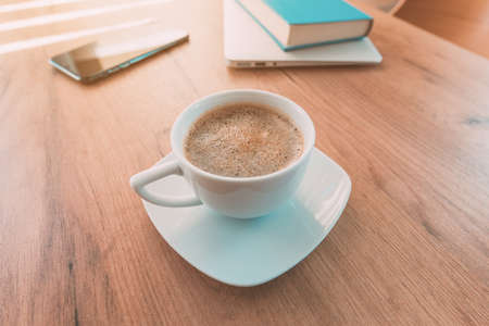 Importance of caffeine and coffee for freelance work. Coffee cup, mobile smart phone, laptop computer and a book on home office table.の写真素材