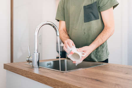 Man washing coffee cup at kitchen sink, selective focus
