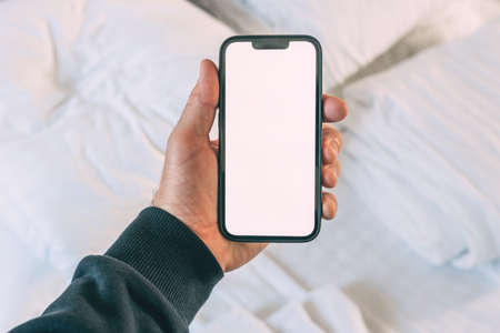 Tourist in hotel bedroom holding smartphone with blank mockup screen for booking and reservation app or accommodation rating serviceの写真素材
