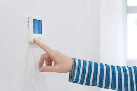 Female hand using of home heating and cooling system control unit, selective focus