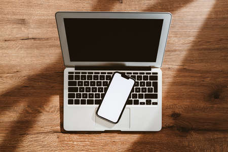 Mobile phone with blank white mockup touchscreen and laptop computer on office desk, top view flat lay with copy space for business communication and connectivity conceptの写真素材