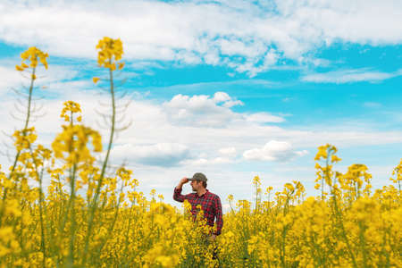 Confident and self-assured farm worker wearing red plaid shirt and trucker's hat standing in...