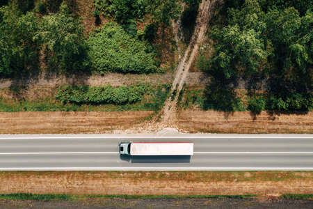 Aerial shot of semi-truck driving along the highway through countryside landscape, drone pov...