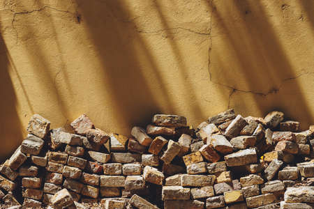 Pile of old bricks stacked in house back yard, leaning on to yellow wall, copy space includedの写真素材