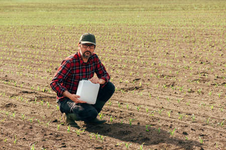 Corn crop protection concept, male farmer agronomist holding jerry can container canister with pesticide, selective focusの写真素材