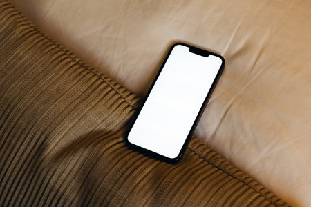 Smartphone with blank white screen as mockup copy space on bed sheetの写真素材