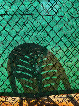 Shadow of a plastic chair on green screening of chain-link fenceの写真素材
