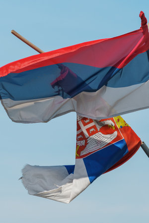 Torn and weathered flag of Serbia on a post waving in wind, selective focus