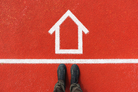 House mortgage concept, top view of man on dirty boots standing over house symbol drawn on tartan...