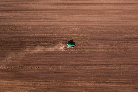 Agricultural tractor with tiller attached performing field tillage before the sowing season, aerial shot seen from the drone pov top downの写真素材