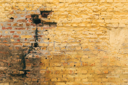 Old cracked and dirty yellow brick wall background with unique worn texture and pattern of the surface as abstract backdrop for designの写真素材