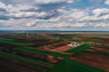 Farm silos in field, aerial view from drone pov on sunny spring day with white clouds over horizon