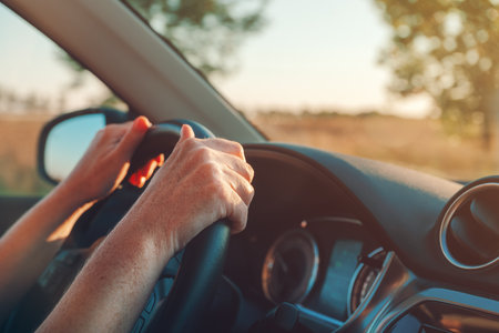Female hands on the vehicle steering wheel, inside the car, driving through countryside, selective...