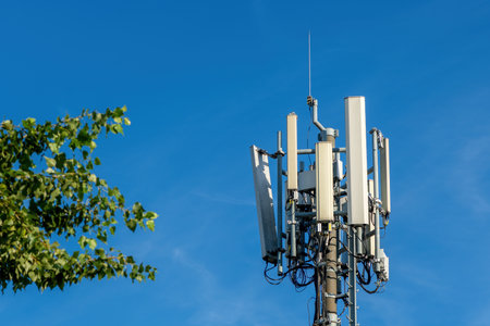 Mobile telephony signal repeater and base station antenna next to a green tree, selective focus
