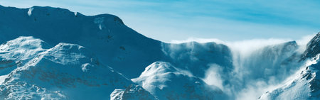Clouds rolling over snowcapped mountain top in Julian Alps range during winter in Slovenia