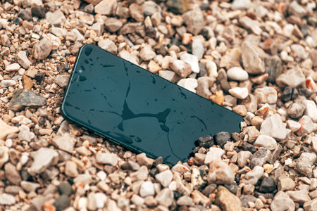 Wet and damaged smartphone in beach pebbles, selective focus