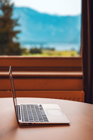 Laptop computer on living room desk by the window with beautiful scenic view of summer landscape, selective focusの写真素材