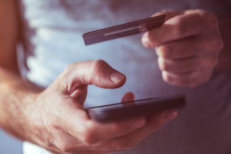 Credit card and mobile phone app online purchase, closeup of male hands using smartphone to complete...