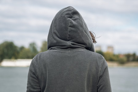 Rear view of woman wearing grey hoodie standing on the river bank in cold autumn morningの写真素材