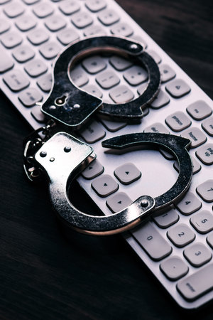 High tech IT cyber crime arrest concept, image of police handcuffs over computer keyboard, selective focusの写真素材