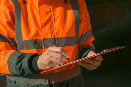 Architect and construction engineer making notes and remarks during building site inspection,...
