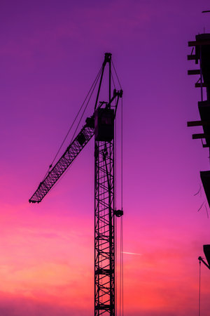 Silhouette of construction crane machinery in purple sunset, vertical imageの写真素材