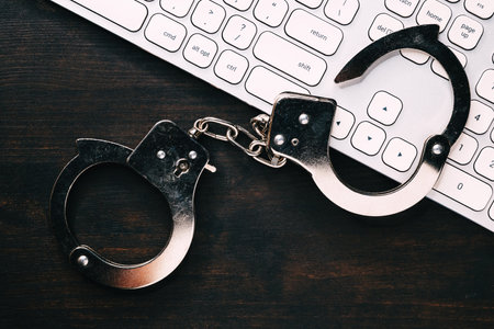 High tech IT cyber crime arrest concept, image of police handcuffs over computer keyboard, selective focusの写真素材