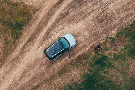 Man lost off-track on countryside road exiting out of the car and looking around, aerial shot from drone pov, top downの写真素材