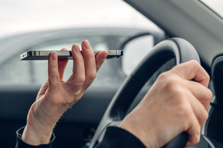 Woman driving car and talking on mobile phone while holding it in front of her mouth, communication...