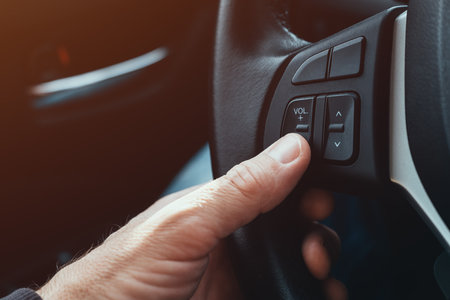 Driver pushing volume down button on car steering wheel, selective focus