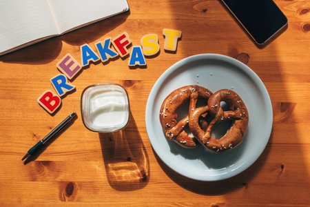 Smartphone, notebook and pen on breakfast table with pretzels and yoghurt, top view