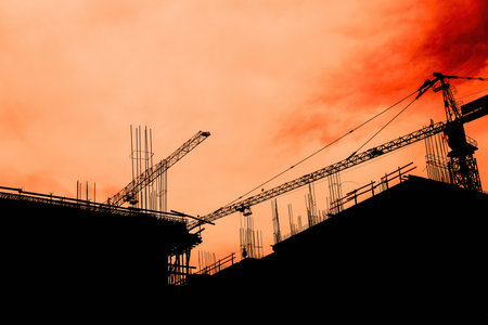 Residential building development and construction, back lit cranes and scaffold with orange skyの写真素材