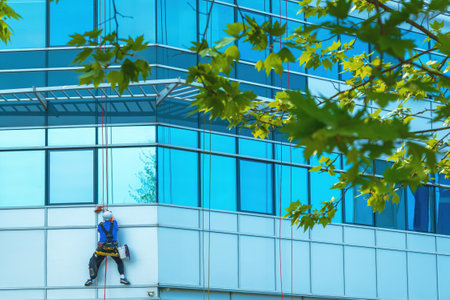 Window washer cleaning facade of modern office building, selective focus